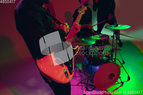 Image of Young caucasian musician, band performing in neon light on red studio background