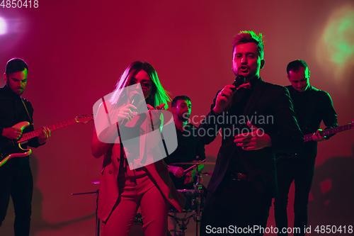 Image of Young caucasian musicians, band performing in neon light on red studio background