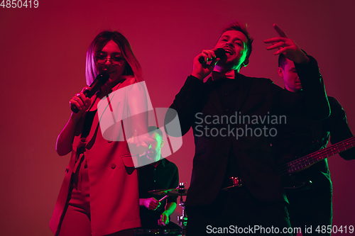 Image of Young caucasian musicians, singers performing in neon light on red studio background