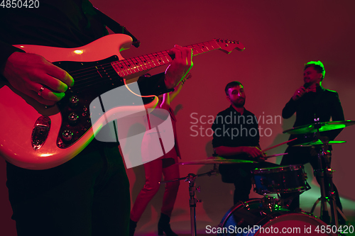 Image of Young caucasian musicians, band performing in neon light on red studio background