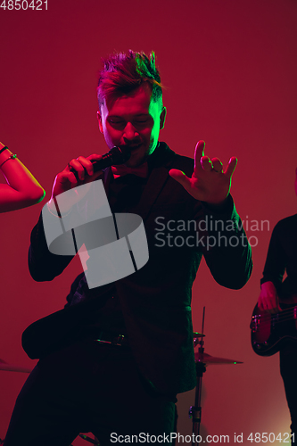 Image of Young caucasian musician, singer performing in neon light on red studio background