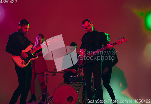 Image of Young caucasian musicians, band performing in neon light on red studio background