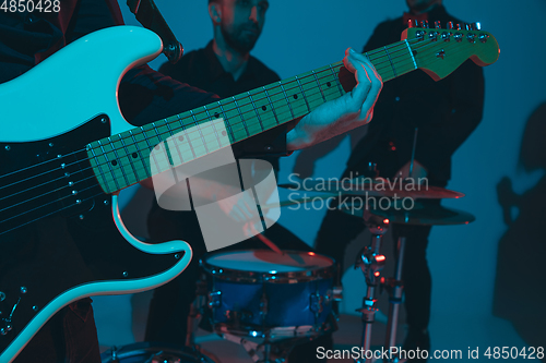 Image of Young caucasian musicians, band performing in neon light on blue studio background, guitarist in front