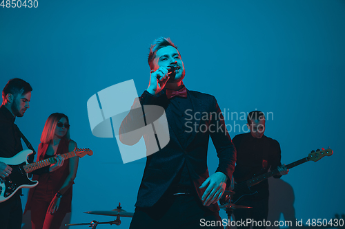 Image of Young caucasian musicians, band performing in neon light on blue studio background, singer in front