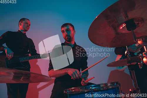 Image of Young caucasian musicians, band performing in neon light on blue studio background