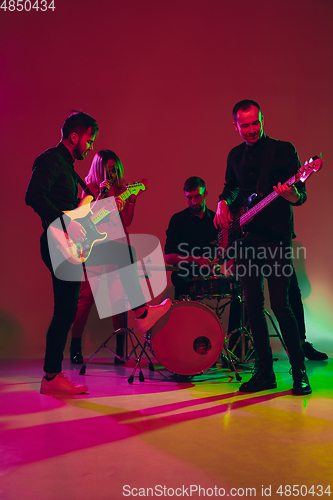 Image of Young caucasian musicians, band performing in neon light on red studio background