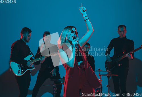 Image of Young caucasian musicians, band performing in neon light on blue studio background, singer in front