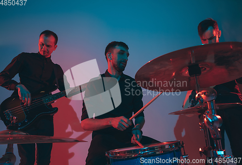 Image of Young caucasian musicians, band performing in neon light on blue studio background