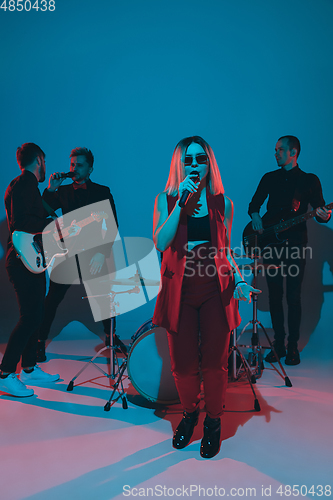 Image of Young caucasian musicians, band performing in neon light on blue studio background, singer in front