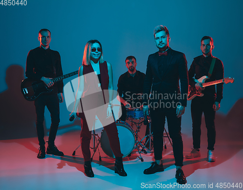 Image of Young caucasian musicians, band performing in neon light on blue studio background