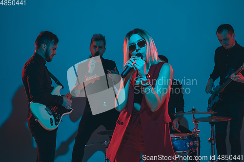 Image of Young caucasian musicians, band performing in neon light on blue studio background, singer in front