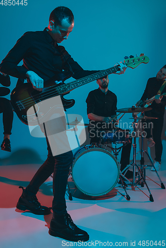 Image of Young caucasian musicians, band performing in neon light on blue studio background, guitarist in front