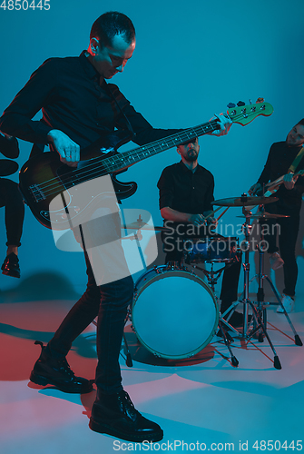 Image of Young caucasian musicians, band performing in neon light on blue studio background, guitarist in front