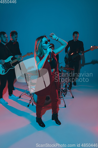 Image of Young caucasian musicians, band performing in neon light on blue studio background, singer in front