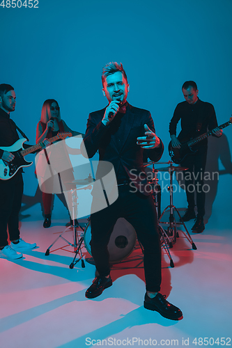 Image of Young caucasian musicians, band performing in neon light on blue studio background, singer in front