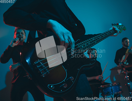 Image of Young caucasian musicians, band performing in neon light on blue studio background, guitarist in front