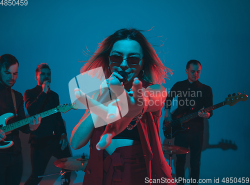 Image of Young caucasian musicians, band performing in neon light on blue studio background, singer in front