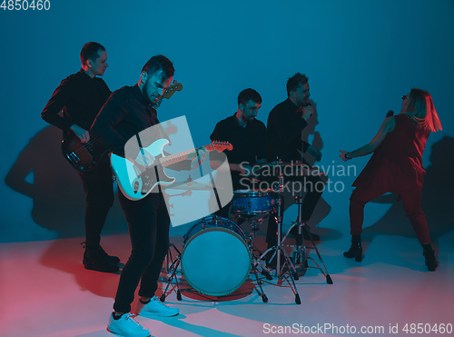 Image of Young caucasian musicians, band performing in neon light on blue studio background, guitarist in front