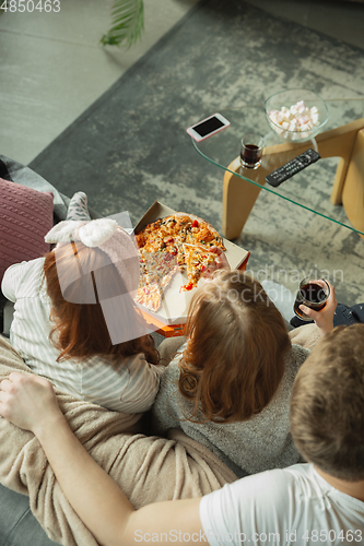 Image of Family spending nice time together at home, looks happy and cheerful, eating pizza. Top view.