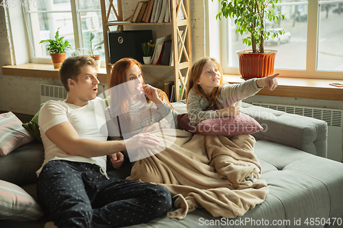 Image of Family spending nice time together at home, looks happy and excited, eating pizza, watching sport match