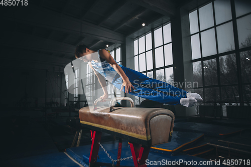 Image of Little male gymnast training in gym, flexible and active. Caucasian fit little boy, athlete in sportswear practicing in exercises for strength, balance.