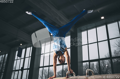 Image of Little male gymnast training in gym, flexible and active. Caucasian fit little boy, athlete in sportswear practicing in exercises for strength, balance.