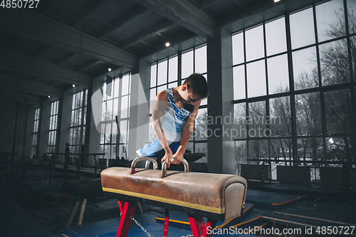 Image of Little male gymnast training in gym, flexible and active. Caucasian fit little boy, athlete in sportswear practicing in exercises for strength, balance.