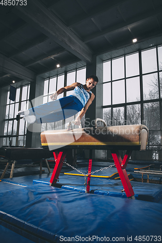 Image of Little male gymnast training in gym, flexible and active. Caucasian fit little boy, athlete in sportswear practicing in exercises for strength, balance.