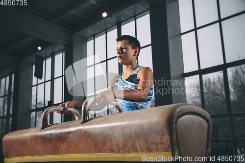Image of Little male gymnast training in gym, flexible and active. Caucasian fit little boy, athlete in sportswear practicing in exercises for strength, balance.