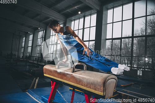 Image of Little male gymnast training in gym, flexible and active. Caucasian fit little boy, athlete in sportswear practicing in exercises for strength, balance.