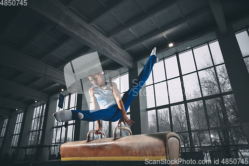 Image of Little male gymnast training in gym, flexible and active. Caucasian fit little boy, athlete in sportswear practicing in exercises for strength, balance.