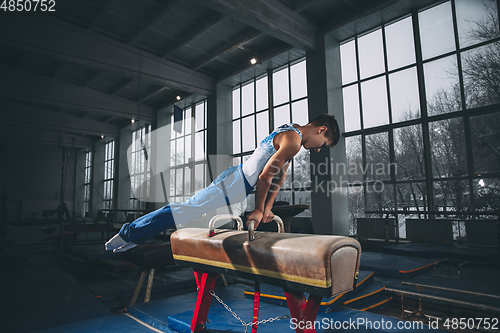 Image of Little male gymnast training in gym, flexible and active. Caucasian fit little boy, athlete in sportswear practicing in exercises for strength, balance.