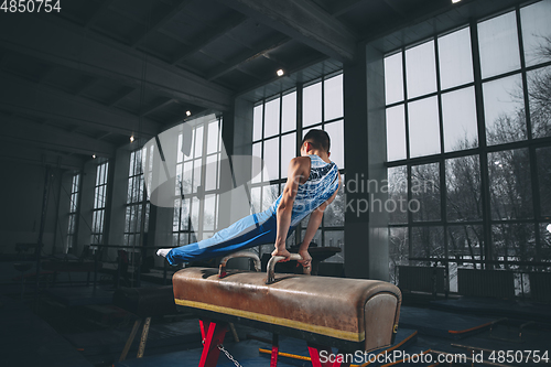 Image of Little male gymnast training in gym, flexible and active. Caucasian fit little boy, athlete in sportswear practicing in exercises for strength, balance.