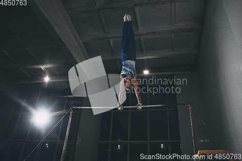 Image of Little male gymnast training in gym, flexible and active. Caucasian fit little boy, athlete in sportswear practicing in exercises for strength, balance.