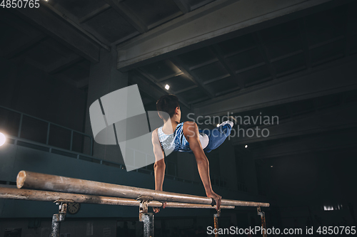 Image of Little male gymnast training in gym, flexible and active. Caucasian fit little boy, athlete in sportswear practicing in exercises for strength, balance.