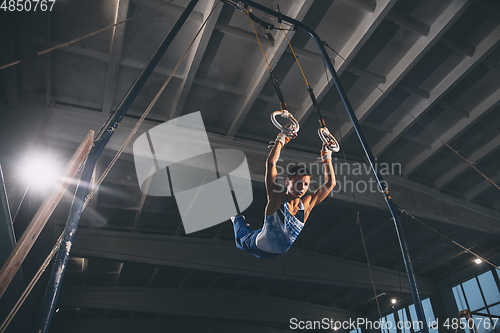 Image of Little male gymnast training in gym, flexible and active. Caucasian fit little boy, athlete in sportswear practicing in exercises for strength, balance.