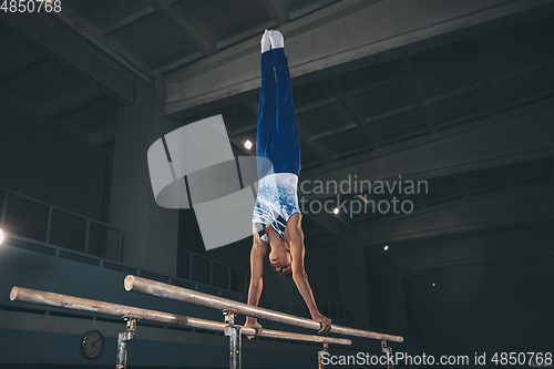 Image of Little male gymnast training in gym, flexible and active. Caucasian fit little boy, athlete in sportswear practicing in exercises for strength, balance.