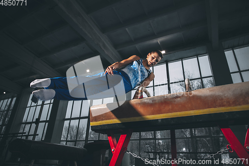 Image of Little male gymnast training in gym, flexible and active. Caucasian fit little boy, athlete in sportswear practicing in exercises for strength, balance.