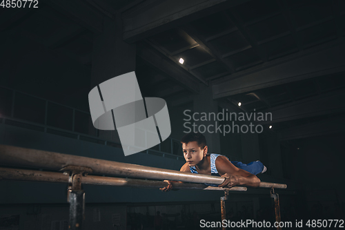 Image of Little male gymnast training in gym, flexible and active. Caucasian fit little boy, athlete in sportswear practicing in exercises for strength, balance.