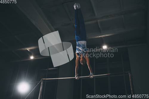 Image of Little male gymnast training in gym, flexible and active. Caucasian fit little boy, athlete in sportswear practicing in exercises for strength, balance.