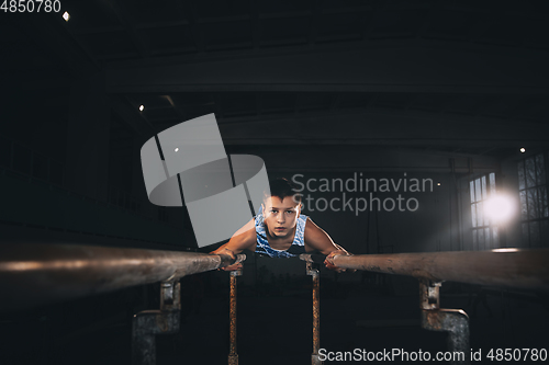 Image of Little male gymnast training in gym, flexible and active. Caucasian fit little boy, athlete in sportswear practicing in exercises for strength, balance.