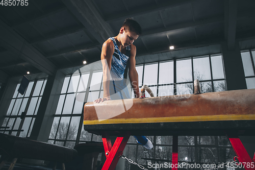 Image of Little male gymnast training in gym, flexible and active. Caucasian fit little boy, athlete in sportswear practicing in exercises for strength, balance.