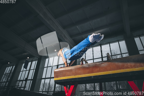 Image of Little male gymnast training in gym, flexible and active. Caucasian fit little boy, athlete in sportswear practicing in exercises for strength, balance.