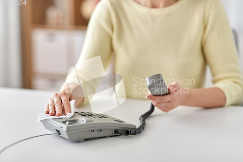 Image of close up of woman cleaning desk phone with tissue