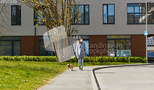 Image of woman in mask and gloves with dog walking in city