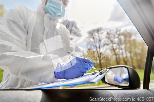 Image of doctor in hazmat suit with clipboard at car