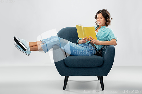 Image of happy young woman in armchair reading book