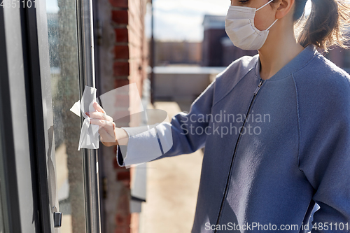 Image of woman in mask cleaning door handle with wet wipe