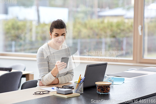 Image of woman with smartphone and laptop at home office