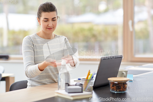 Image of woman spraying hand sanitizer at home office